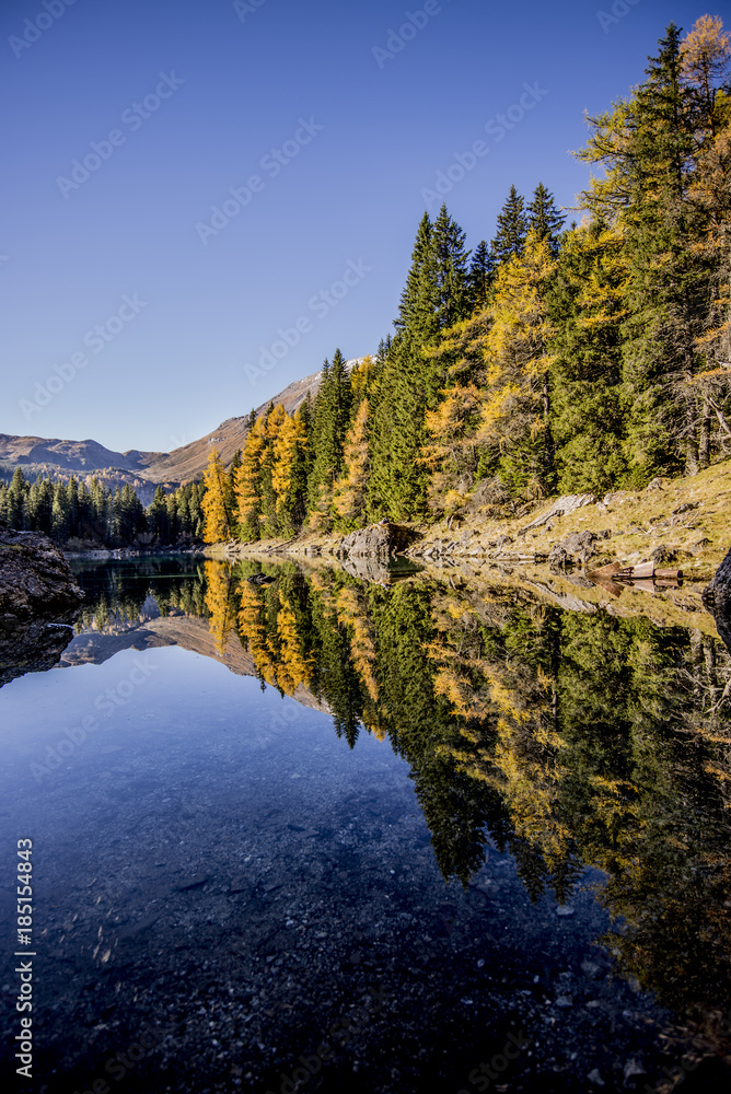 Obernbergersee in autumn with a surface reflection and a blue sky