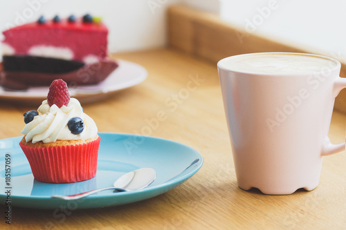 Small cupcake with raspberry and blueberry on the plate, cup of hot cappuccino