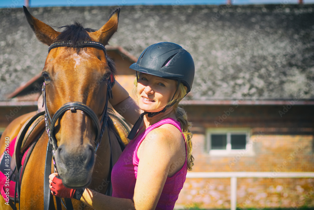 Obraz premium Rider woman talking to her horse. Portrait of riding horse with woman in helmet. Stable in background.