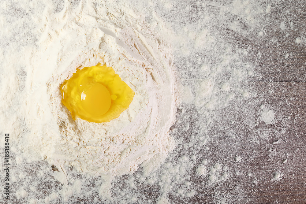 The top view of an egg, beaten into flour, cooking dough against the background of a wooden table. Flat lay The top view of an egg, beaten into flour, cooking dough against the background of a wooden table. Flat lay