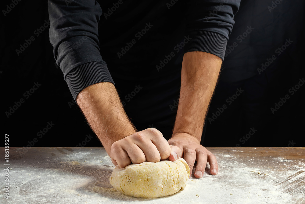 Male hands chef close-up, knead the dough, cook the dough on a dark background.