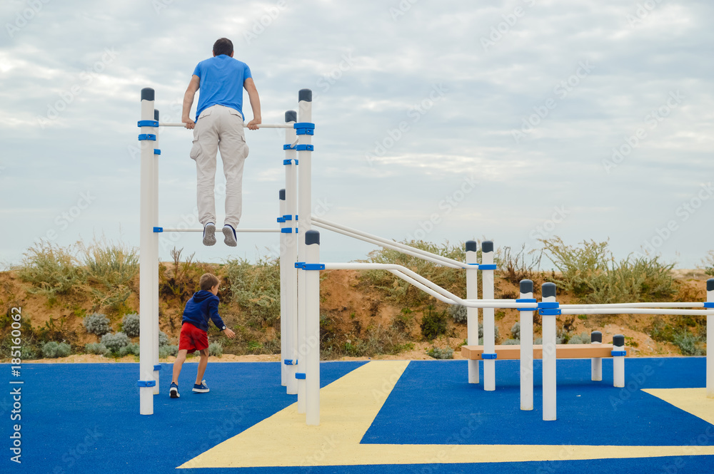 Fototapeta premium Back view of active man exercising doing pull-up using horizontal bar on nature garden outdoors background. Healthy looking person enjoying sportive action lifestyle