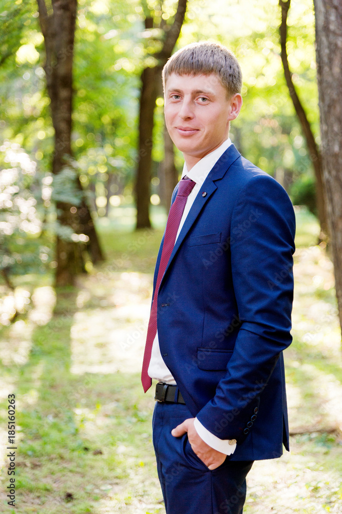 Portrait of a young groom in a blue suit and a red tie at a wedding walk Portrait of a young groom in a blue suit and a red tie at a wedding walk
