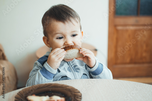 The child is small and cute eating a sandwich with bread sausage and cheese photo