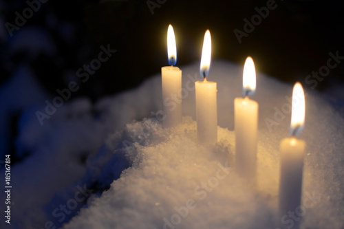 Four burning candles of white candles outdoor in the snow