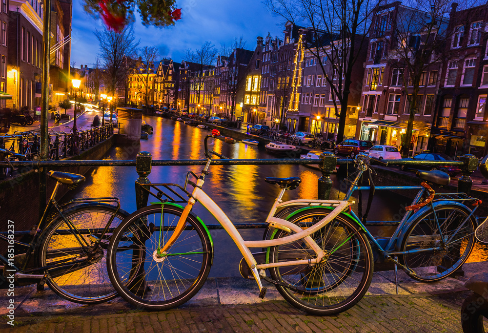 Night illumination of Amsterdam canal and bridge with typical dutch houses, boats and bicycles.