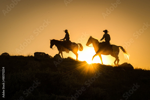 Silhouetted western cowboy and cowgirl on horseback against yellow sunset  photo
