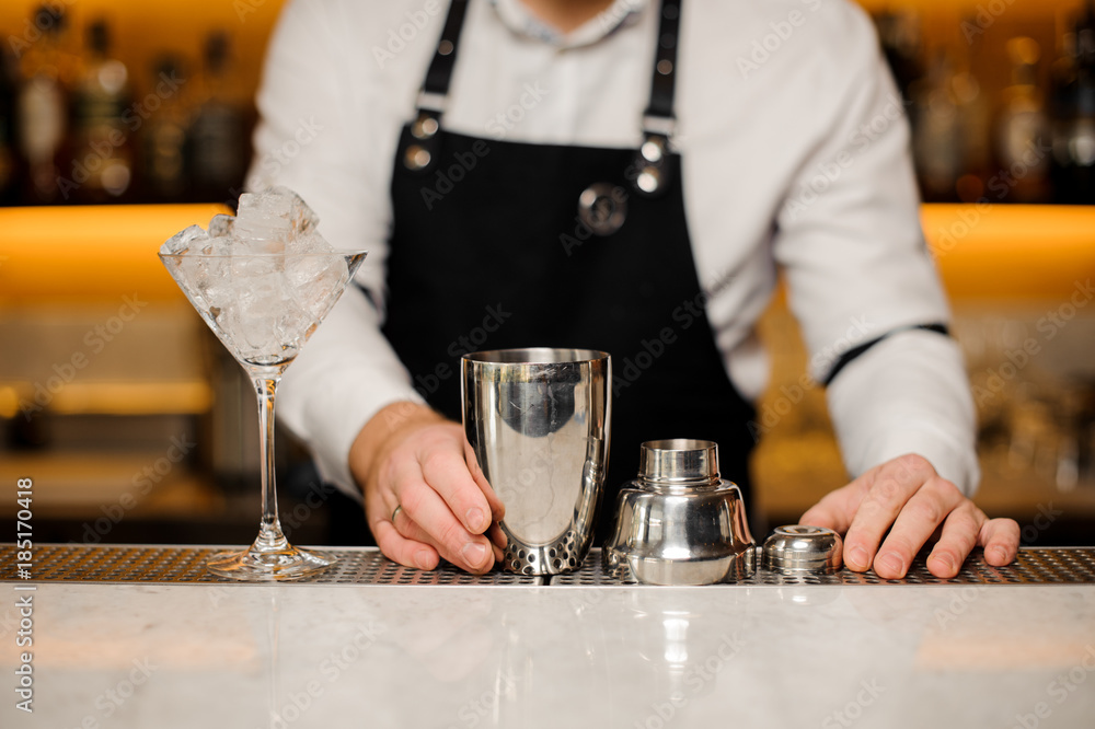 Bartender standing near bar counter with cocktail glass and shaker