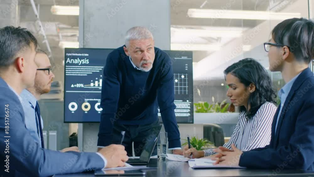 Senior Executive Explains Company's Vision and Potential to His Employees, Leans on the Table. They are Sitting at Big Table in Meeting Room. Shot on RED EPIC-W 8K Helium Cinema Camera. Senior Executive Explains Company's Vision and Potential to His Employees, Leans on the Table. They are Sitting at Big Table in Meeting Room. Shot on RED EPIC-W 8K Helium Cinema Camera.