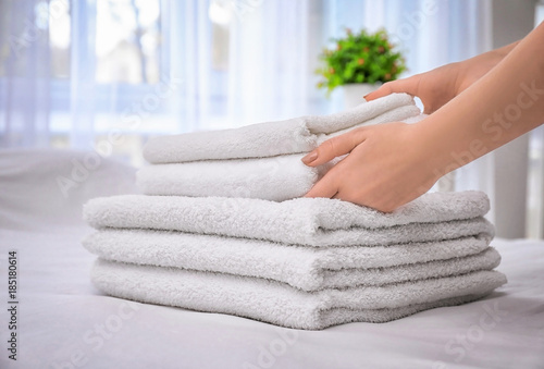 Woman putting white bath towels on bed indoors