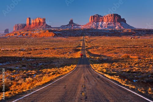 Obraz na płótnie A road leading to Monument Valley with red truck going at camera, Usa