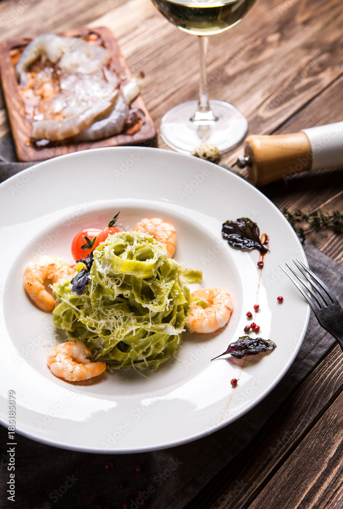Green pasta with shrimps in a white plate on a dark wooden background top view Green pasta with shrimps in a white plate on a dark wooden background top view