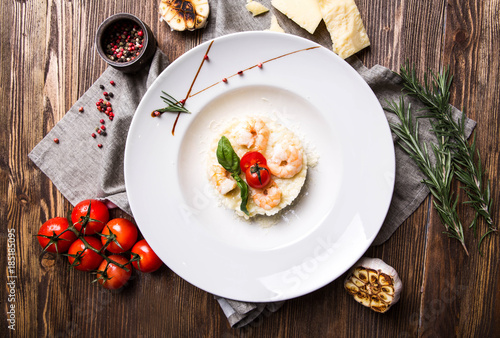 Risotto with shrimps in a white plate on a dark wooden background top view