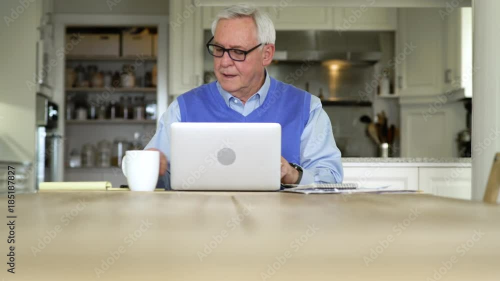 Senior man using a laptop in a dining room Senior man using a laptop in a dining room