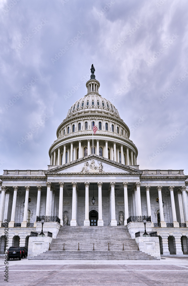 Fototapeta premium Capitol Building facade and empty plaza on a dark cloudy day with two secret service vehicles parked, but no people visible, Washington D.C., USA
