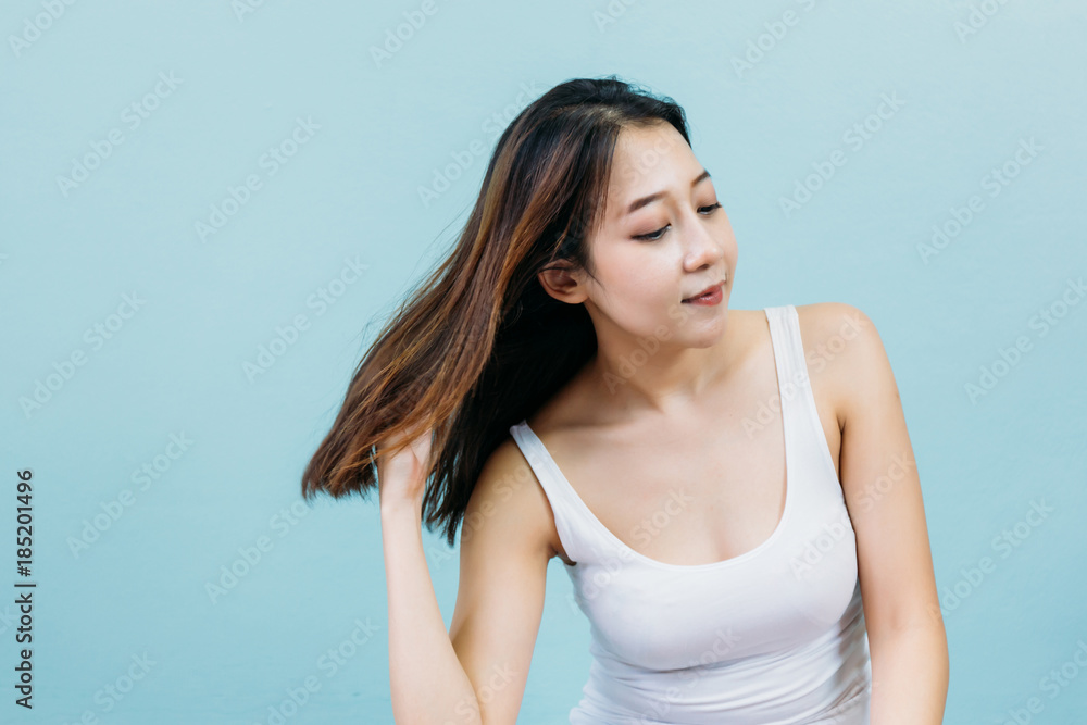 Happy young woman touching her hair against blue pastel background Happy young woman touching her hair against blue pastel background