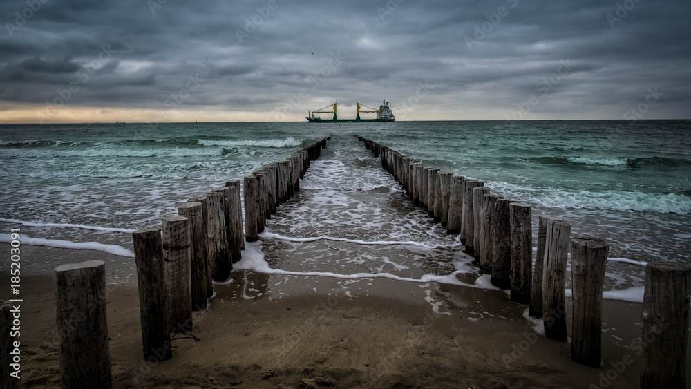 Big ship crossing the wooden pier during cloudy weather at the beach in Vlissingen, Zeeland, Holland, Netherlands