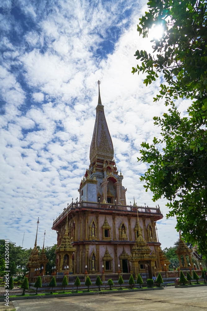Beautiful ornamental sacred white buddhist pagoda spire landscape of Wat Chalong temple with blue sky and white cloud background through green leaves foliage under sunshine