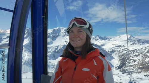 Young woman climbs on a ski slope in the cabin cable car
