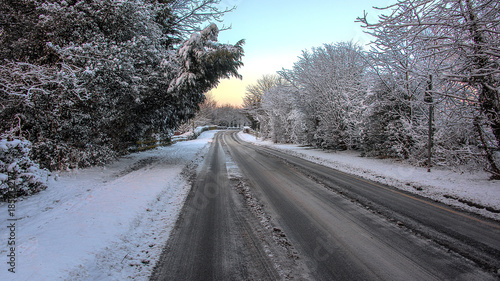 A snow covered winter scene of a country lane just after a snowfall with vehicle tracks in the middle