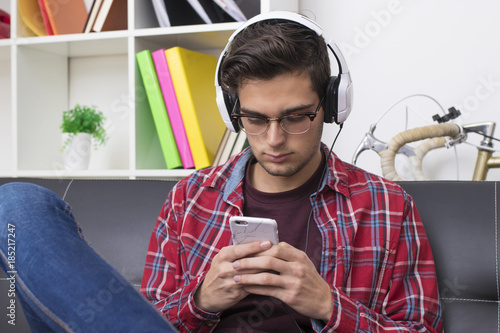 young adult or teenager with mobile phone and headphones at home