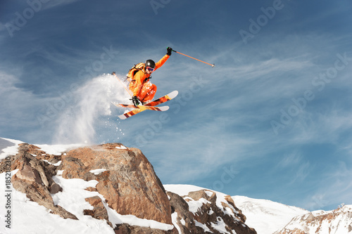 An athlete skier is jumping from high rock high in the mountains.
