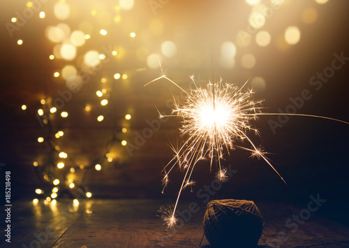 burning sparkler and christmas lights on wooden background