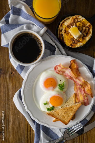 American breakfast with sunny side up eggs, bacon, toast, pancakes, coffee and juice