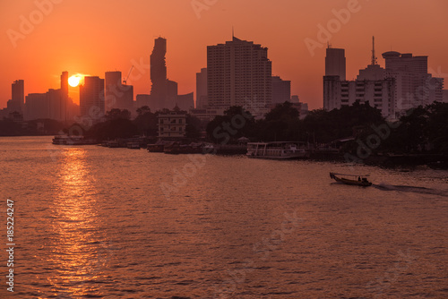 Sunrise over the scenic skyline at Bangkok, Thailand, viewed in backlight at sunrise with orange red clear sky. Boats cruising on the Chao Phraya River. © fabio lamanna