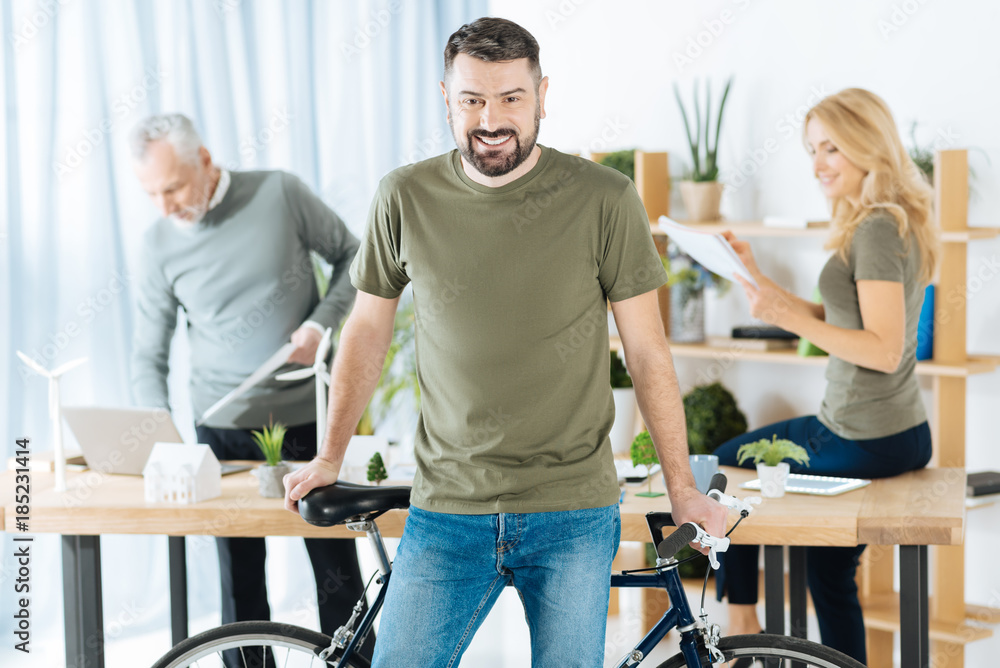 Obraz premium Eco transport. Cheerful emotional young man leaning on his bike while his colleagues standing behind his back and working at the development of alternative energy