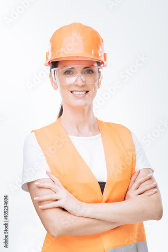 Work done. Happy nice female worker costing arms on the isolated background while  wearing hard hat  and glasses and looking straight  photo