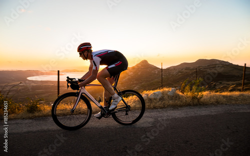 A cyclist does road biking at sunset above the shoreline in Corsica, France.