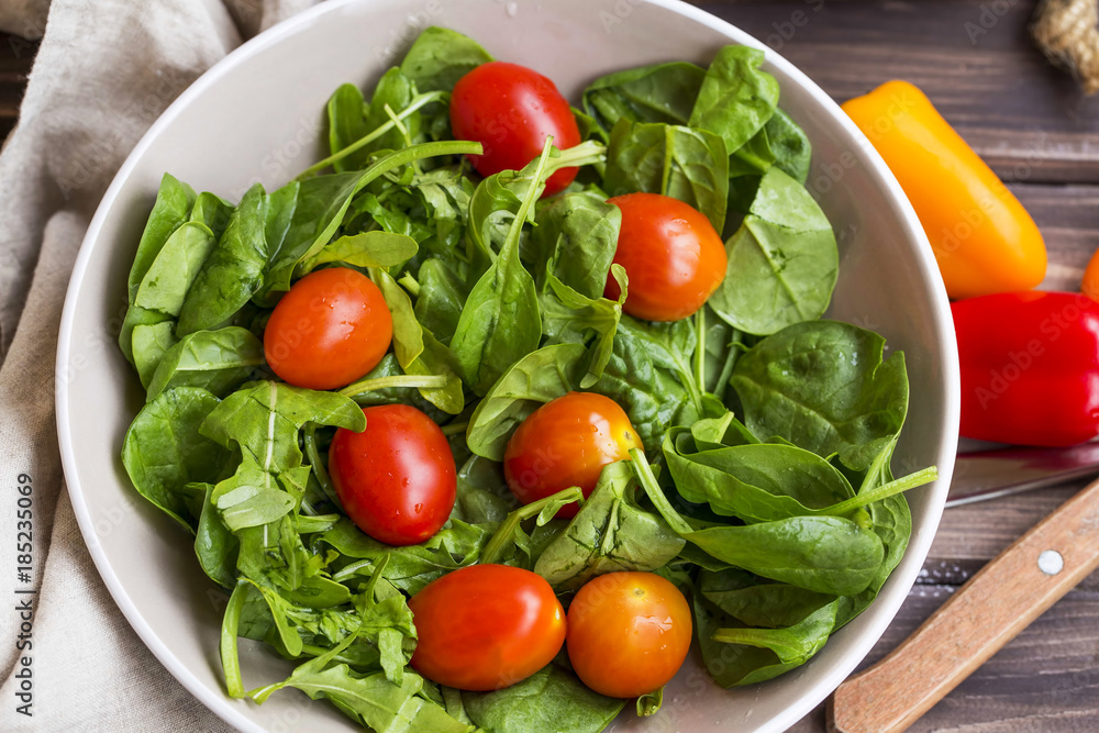 Spring salad closeup with fresh green rocket, spinach leaves and cherry tomatoes , top view