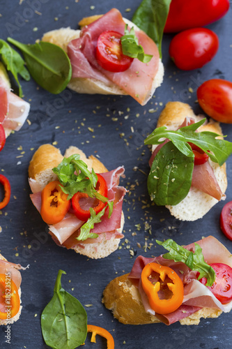 Bruschettas or crostini arrangement with prosciutto ham, green spinach , tomatoes and pepper seasoned with herbs, italian appetizers top view