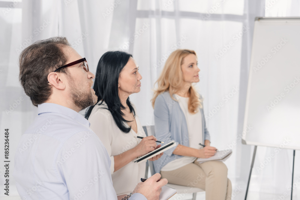 middle aged people with notebooks looking away while sitting at anonymous group therapy middle aged people with notebooks looking away while sitting at anonymous group therapy