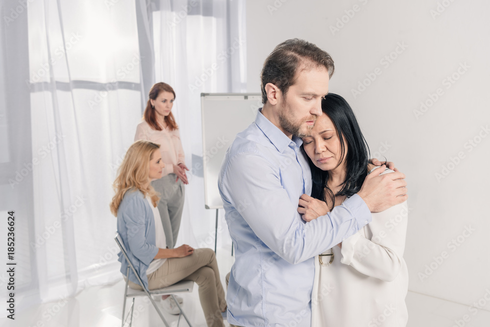 mature man hugging depressed asian woman during group therapy mature man hugging depressed asian woman during group therapy
