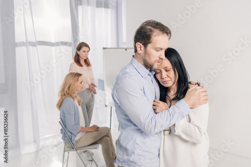 mature man hugging depressed asian woman during group therapy