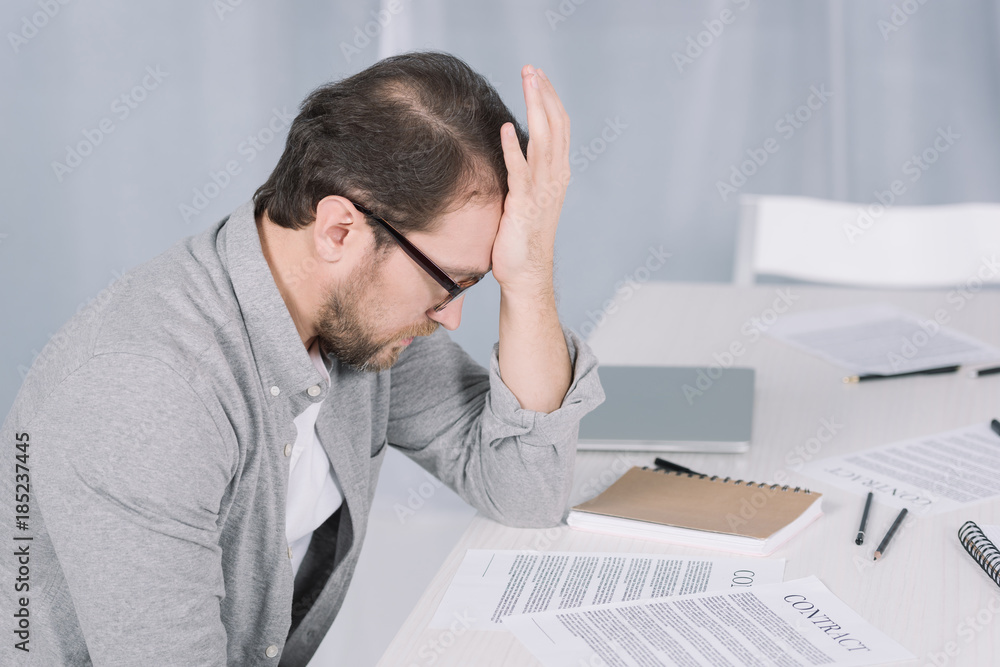 depressed overworked businessman sitting at table with papers in office depressed overworked businessman sitting at table with papers in office