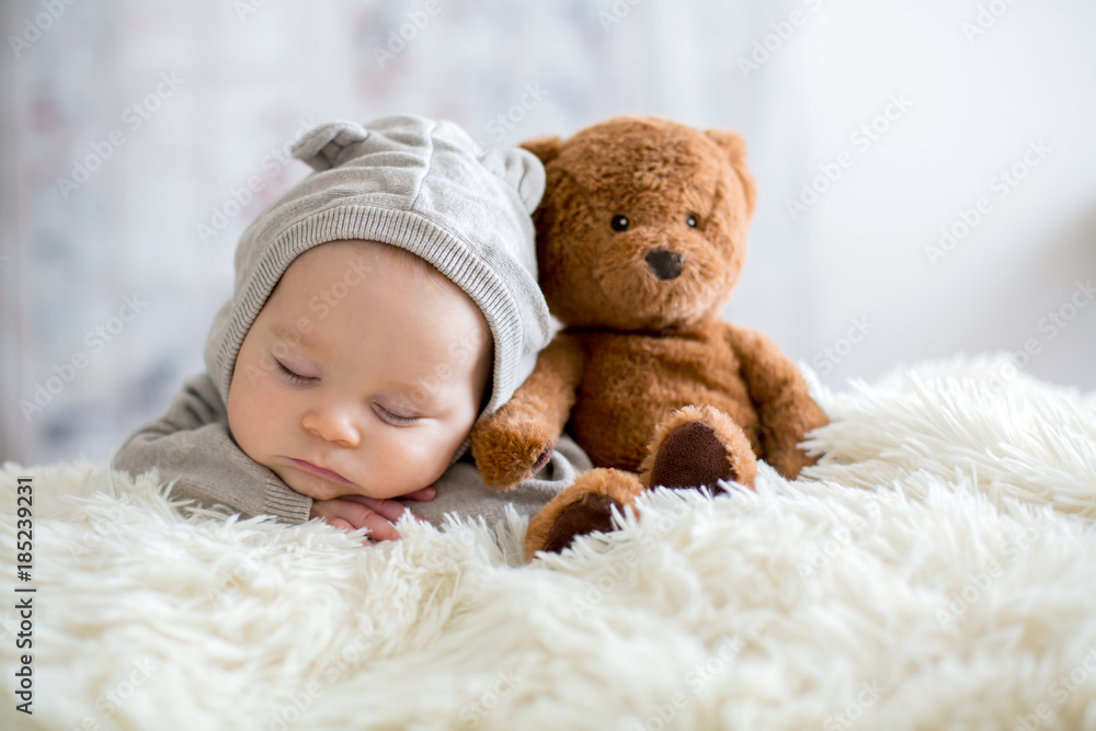 Sweet baby boy in bear overall, sleeping in bed with teddy bear