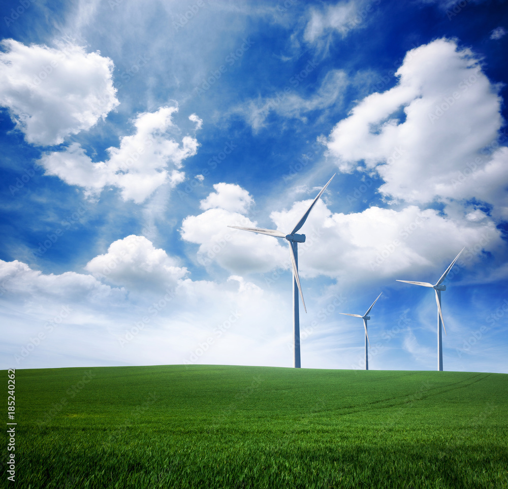 Wind power turbine station on green grass lawn over blue sunny sky