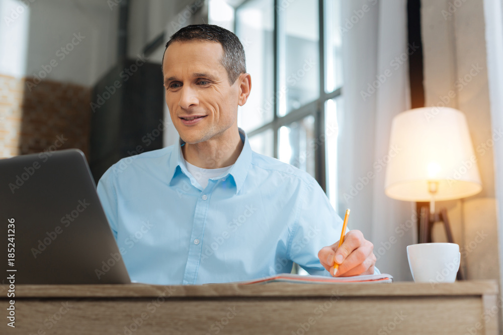 Handsome boss. Cheerful brunette keeping smile on his face and making notes while working at home Handsome boss. Cheerful brunette keeping smile on his face and making notes while working at home