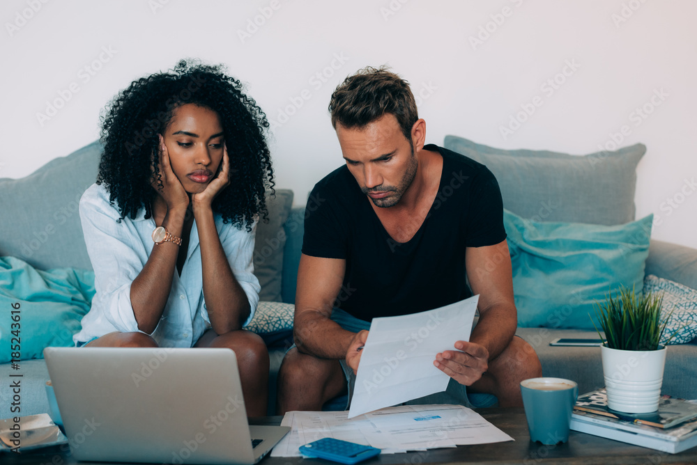 Young interracial couple in the couch stressed with financial problems doing calculations with paper work. Young interracial couple in the couch stressed with financial problems doing calculations with paper work.
