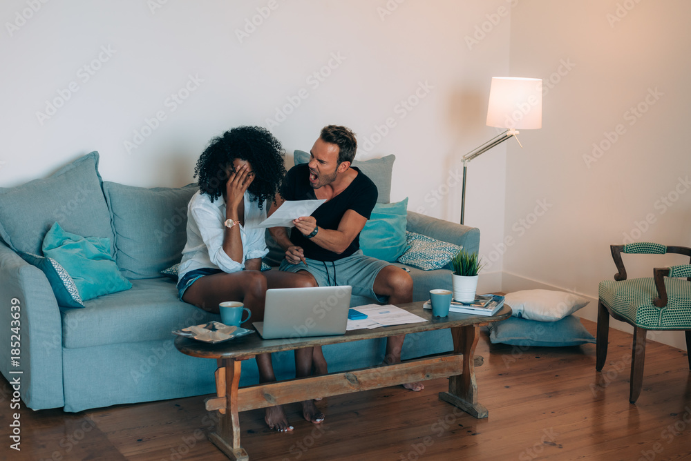 Young interracial couple in the couch stressed with financial problems doing calculations with paper work. Young interracial couple in the couch stressed with financial problems doing calculations with paper work.