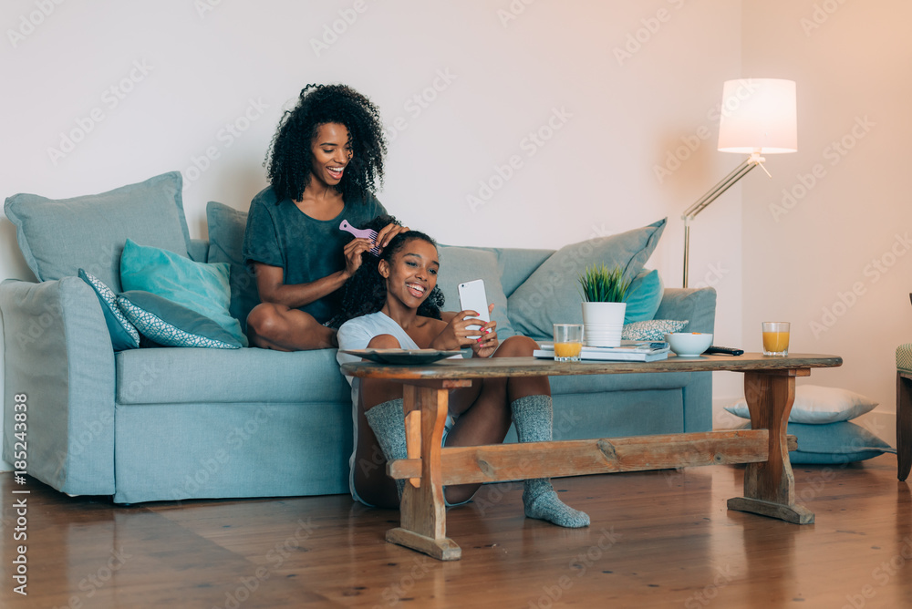 Happy young two black women sitting in the couch combing the hair . Happy young two black women sitting in the couch combing the hair .