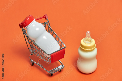 close-up of shopping trolley with baby bottle milk on orange background with some copy space