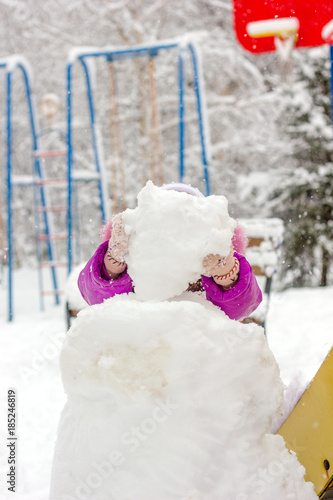 Little kid girl builds snowman on winter day outdoors.