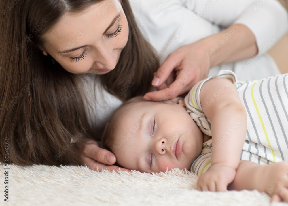 Beautiful young mom looks at baby sleeping in bed at home Beautiful young mom looks at baby sleeping in bed at home