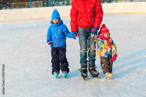 father teaching two kids to skate in winter