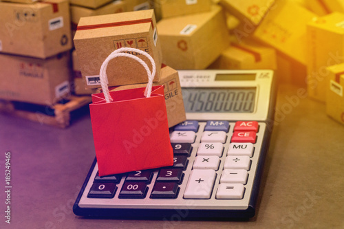 Red paper shopping bag with calculator on pile of cardboard boxes. concept about online shopping or shopping at home or office wherewith customers can purchase goods or services remotely. photo