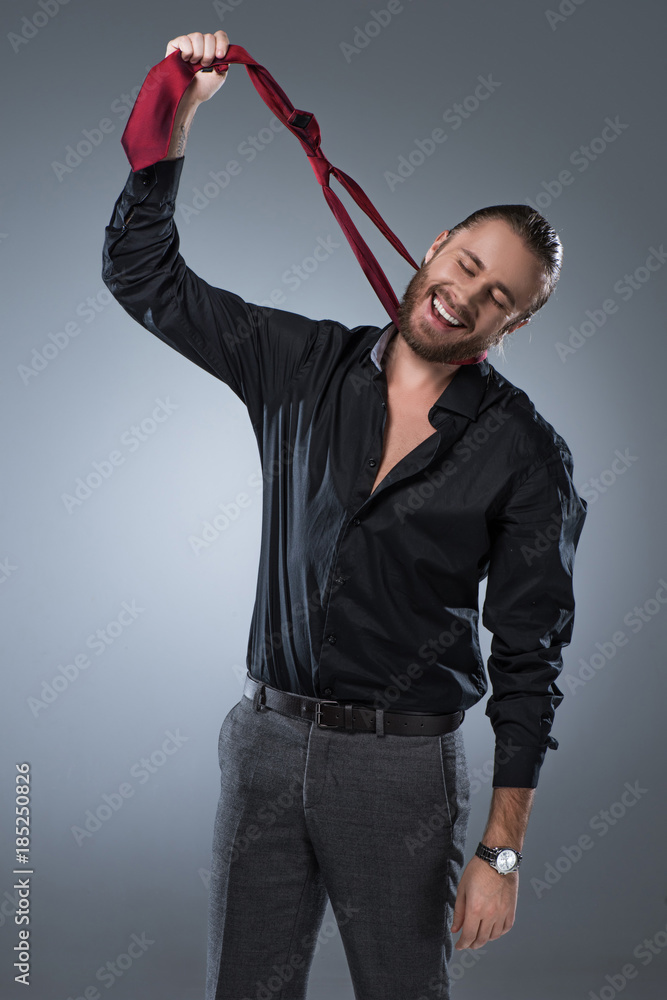 Smiling bearded man in black shirt holding red tie around his neck,  isolated on gray Stock Photo | Adobe Stock